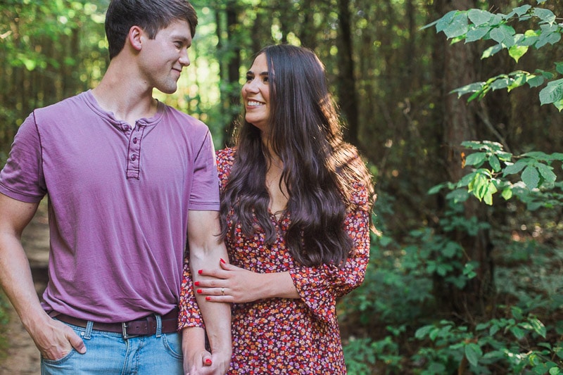 Cute couple holding hands and smiling at each other on trail in the woods at Petit Jean State Park. Photo by Arkansas Wedding Collection.