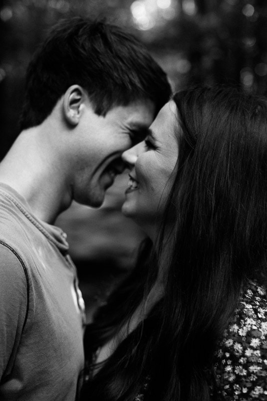 Black and white photo of cute couple laughing while giving an intimate kiss. Photo by Arkansas Wedding Collection.