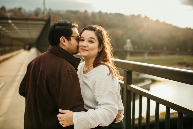Guy kissing fiance's cheek on a bridge